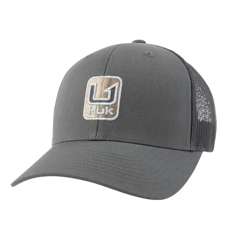 A dark gray trucker hat with a curved brim, featuring a front patch logo that reads 'HUK' and a mesh back.