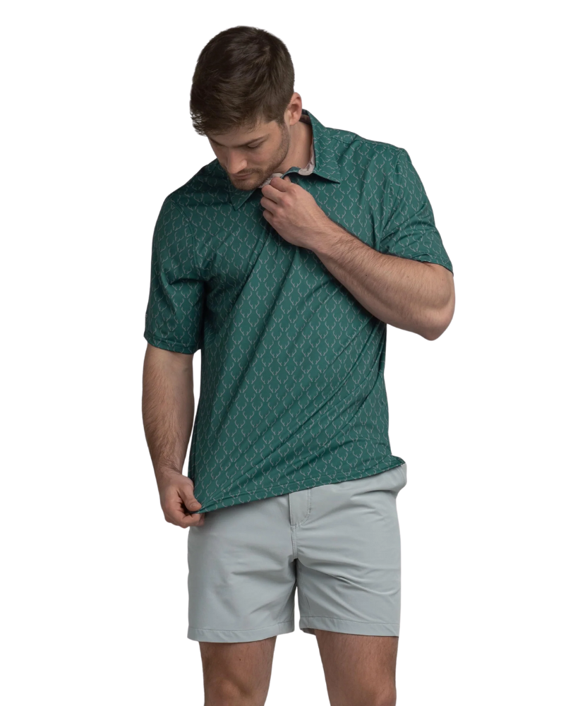 Man wearing a Green polo shirt with deer antler pattern and light gray shorts on a white background