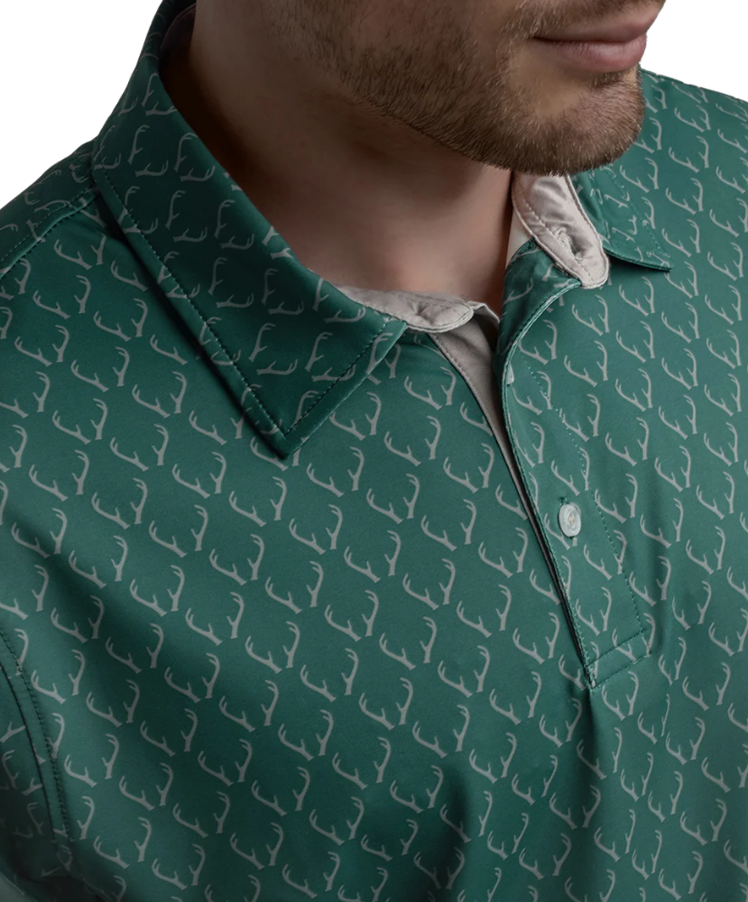 Man wearing a Green polo shirt with deer antler pattern and light gray shorts on a white background