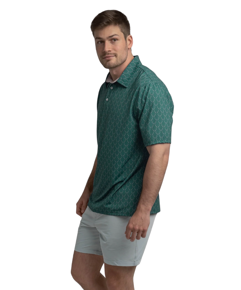 Man wearing a Green polo shirt with deer antler pattern and light gray shorts on a white background