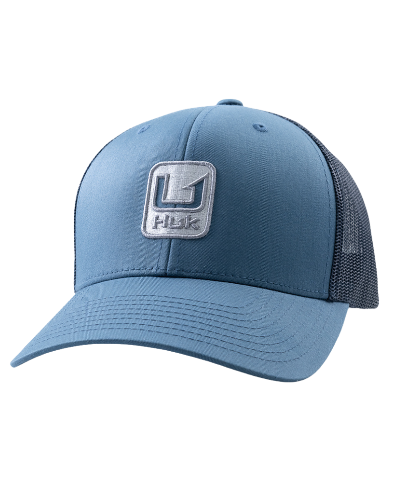 A blue trucker-style baseball cap with a structured front panel, curved brim, and dark mesh back panels. A square embroidered patch on the front displays a stylized 'H' logo above the word 'Huk', indicating the brand.