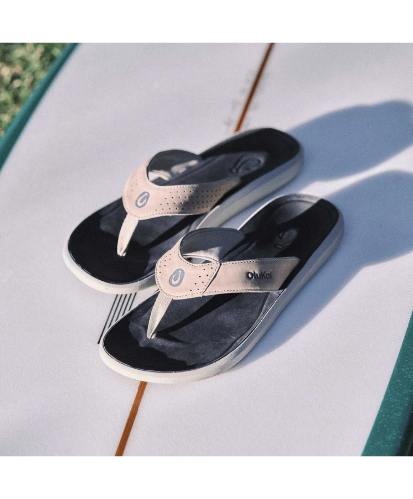 Pair of black and rose gold sandals on a light surface with grass in the background