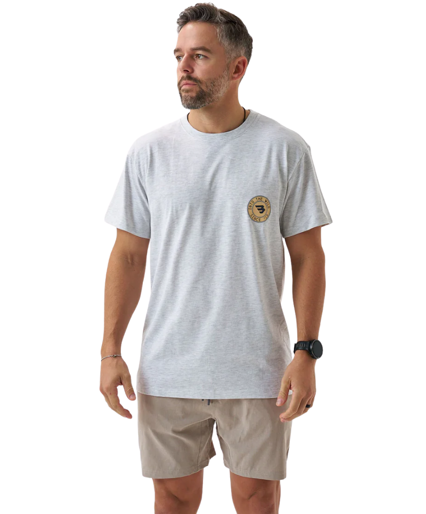 Man wearing a light gray t-shirt with a logo and beige shorts on a white background