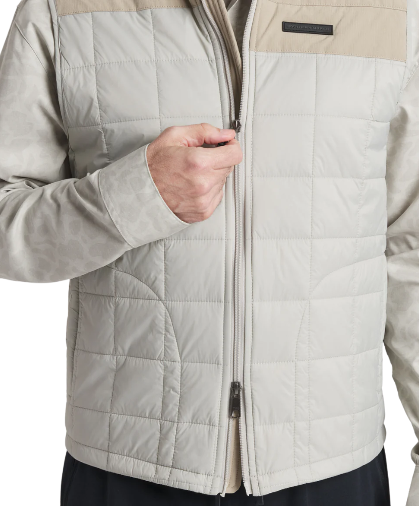 Close-up of a person wearing a beige and gray quilted jacket with a white background