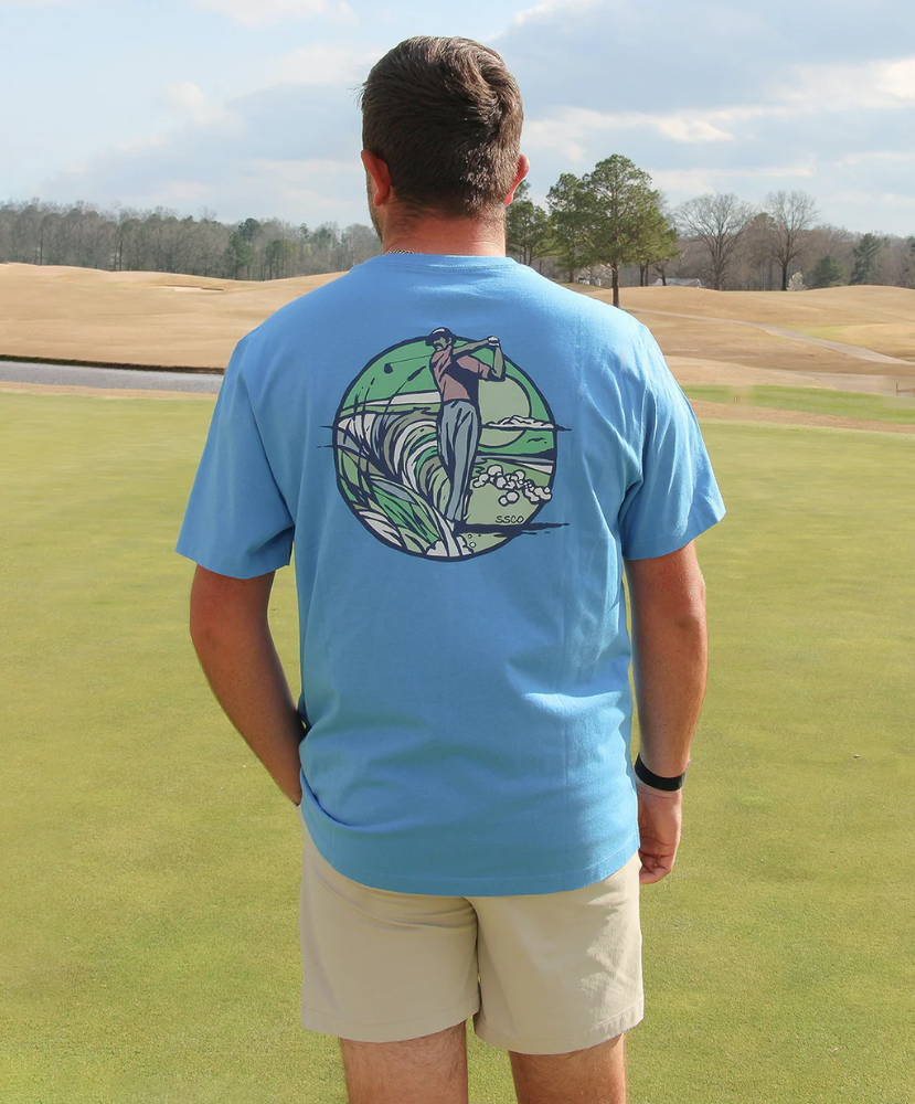 Man wearing a light blue t-shirt with a golf graphic on a golf course