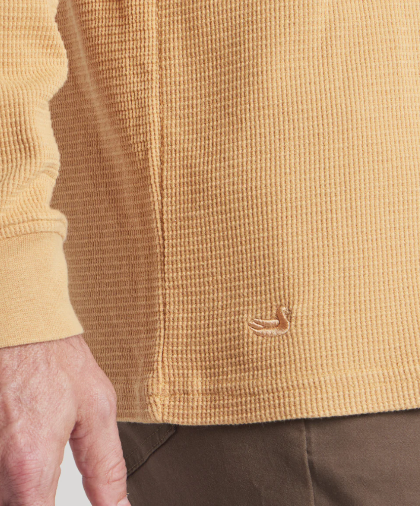 Close-up of a beige textured henley with a small logo on a plain background