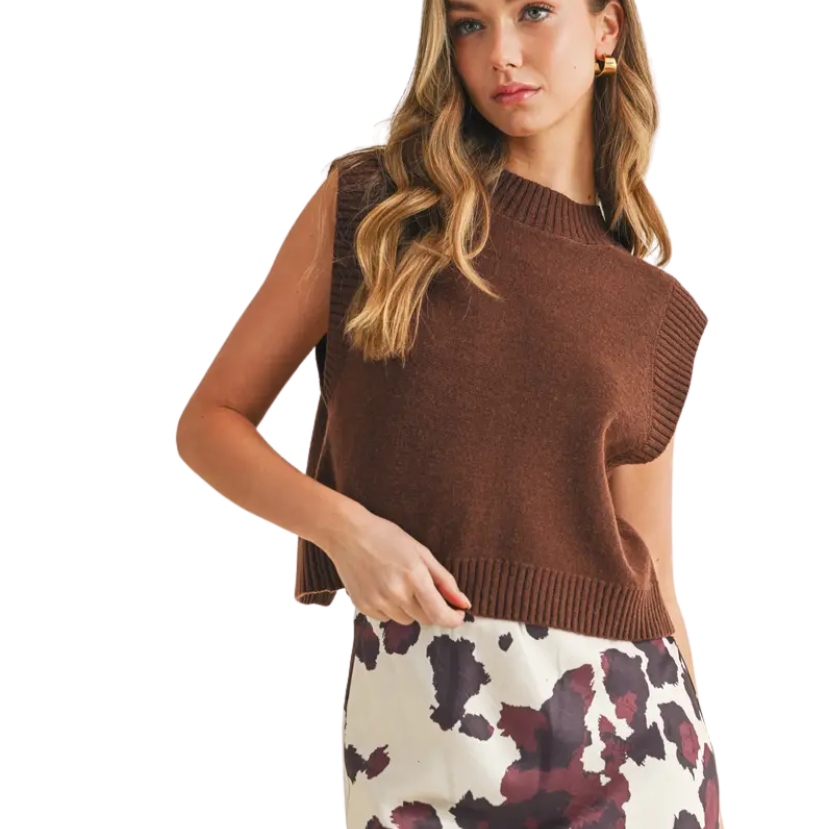 Woman wearing a brown sleeveless sweater with a patterned skirt on a white background