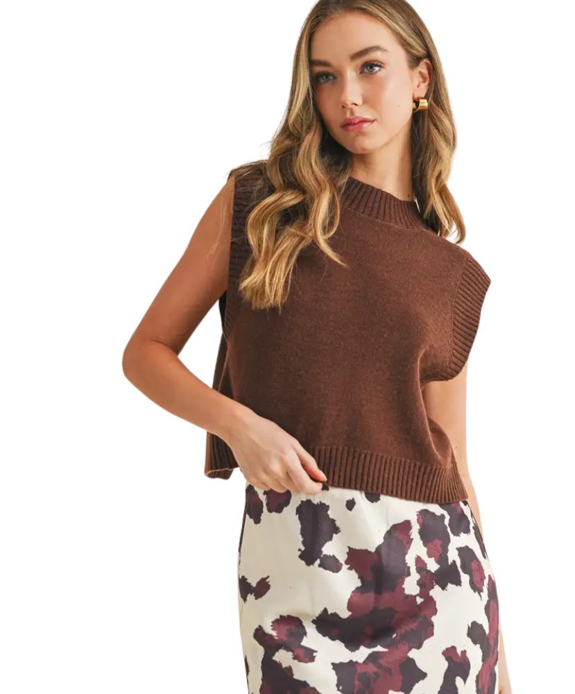 Woman wearing a brown sleeveless sweater with a patterned skirt on a white background