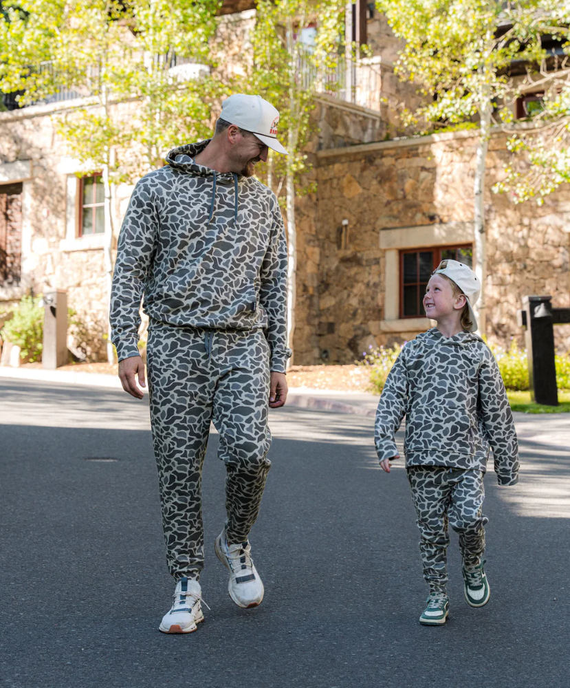 Man and child walking together in matching camouflage outfits on a street.