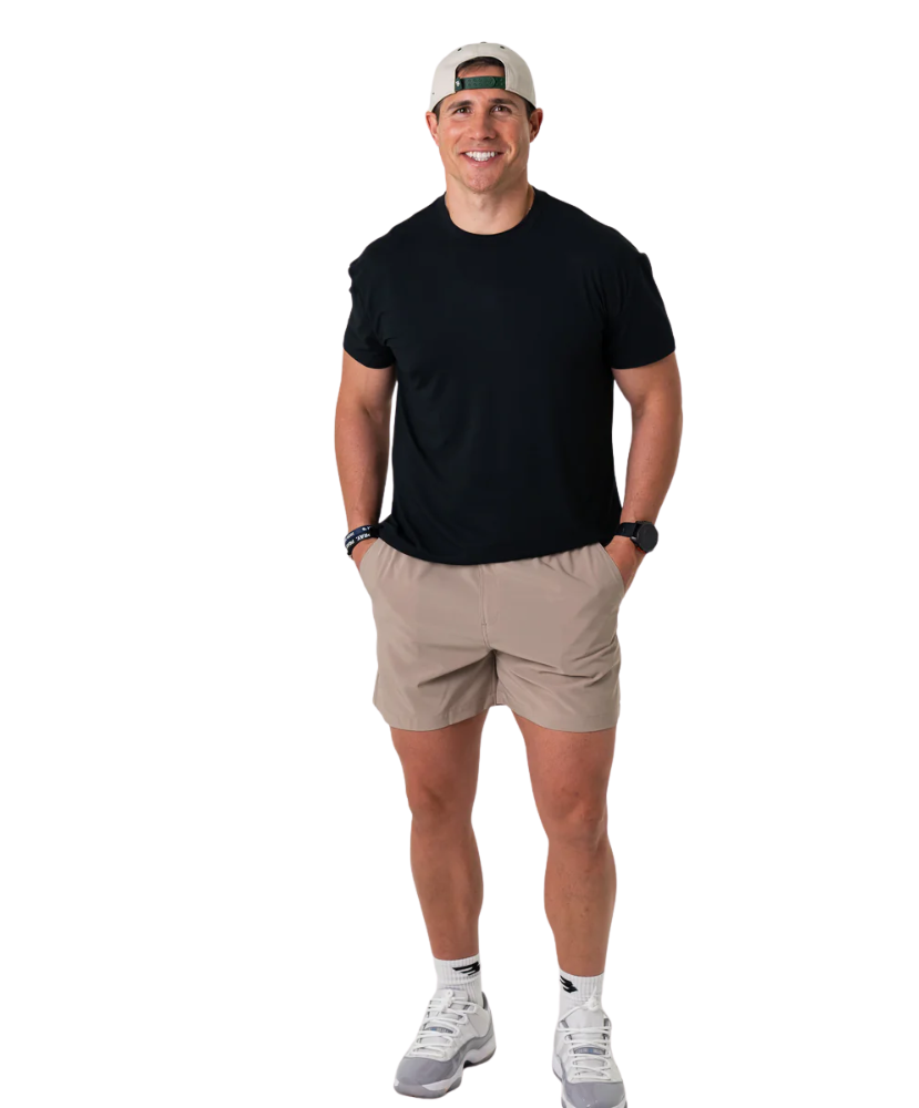 Man wearing a black t-shirt, beige shorts, and a cap on a white background