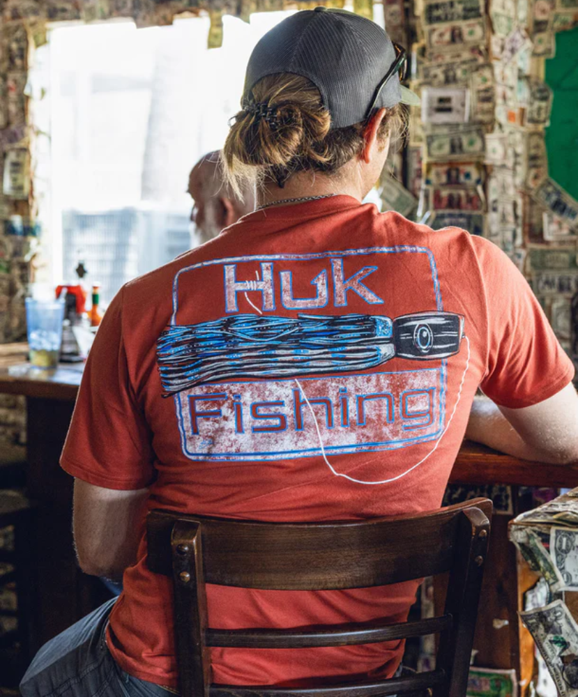 Person wearing a red 'Huk Fishing' shirt sitting in a bar.