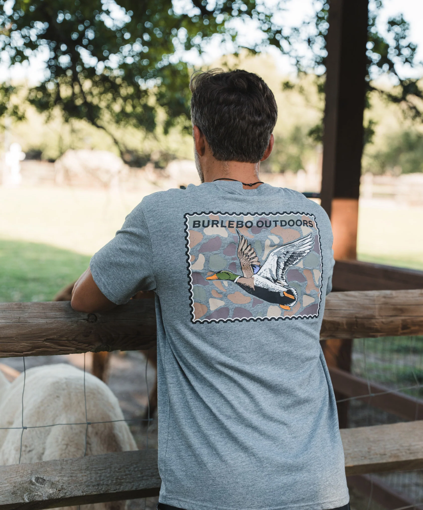 Man wearing a gray t-shirt with a mallard duck graphic and 'Burlebo Outdoors' text, standing outdoors.