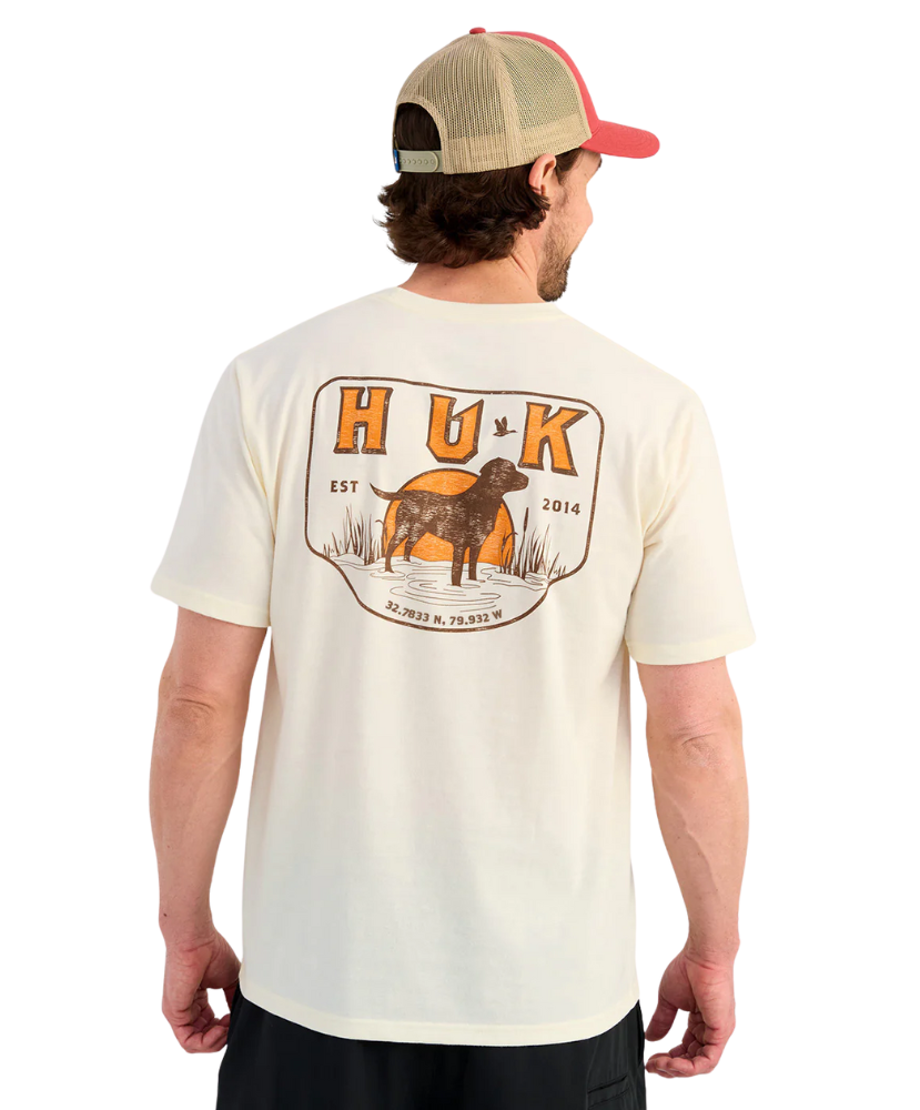 Man wearing a cream t-shirt with a dog graphic and 'HUK' branding on a white background