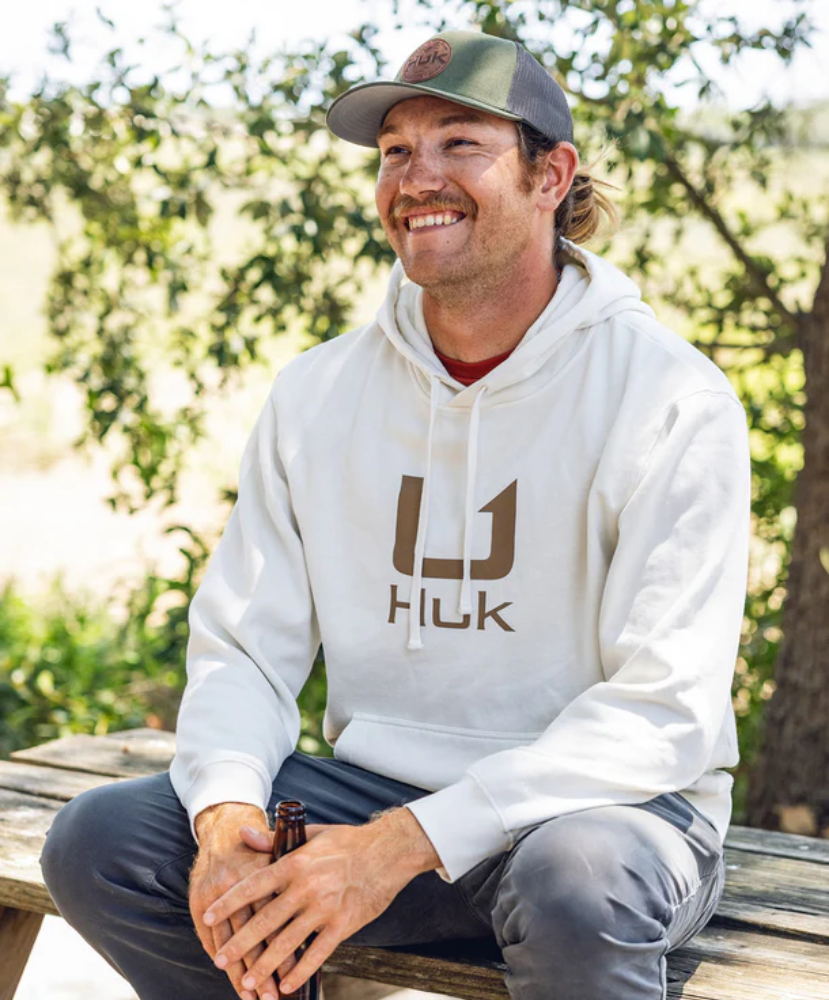 Man wearing a cream hoodie with 'Huk' logo and a cap on