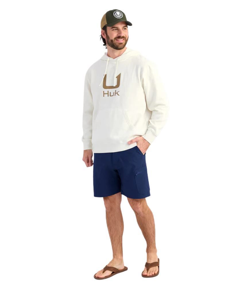 Man wearing a cream hoodie with 'Huk' logo and a cap on a white background