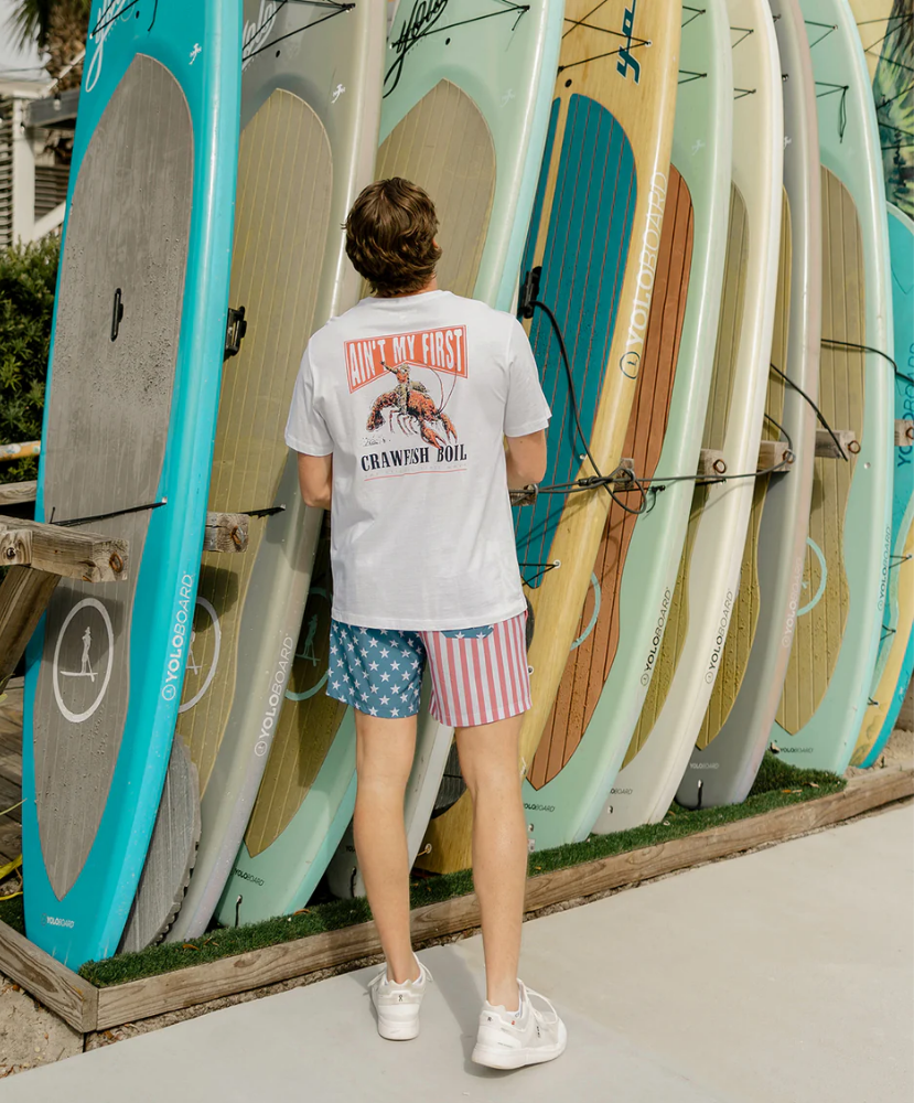 Person standing in front of a display of surfboards wearing a white t-shirt and colorful shorts.