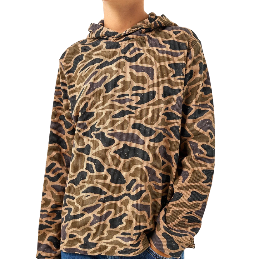 A child wearing a long-sleeve hooded shirt with an allover camouflage-style pattern in tan, brown, and black, paired with blue jeans against a plain white background.