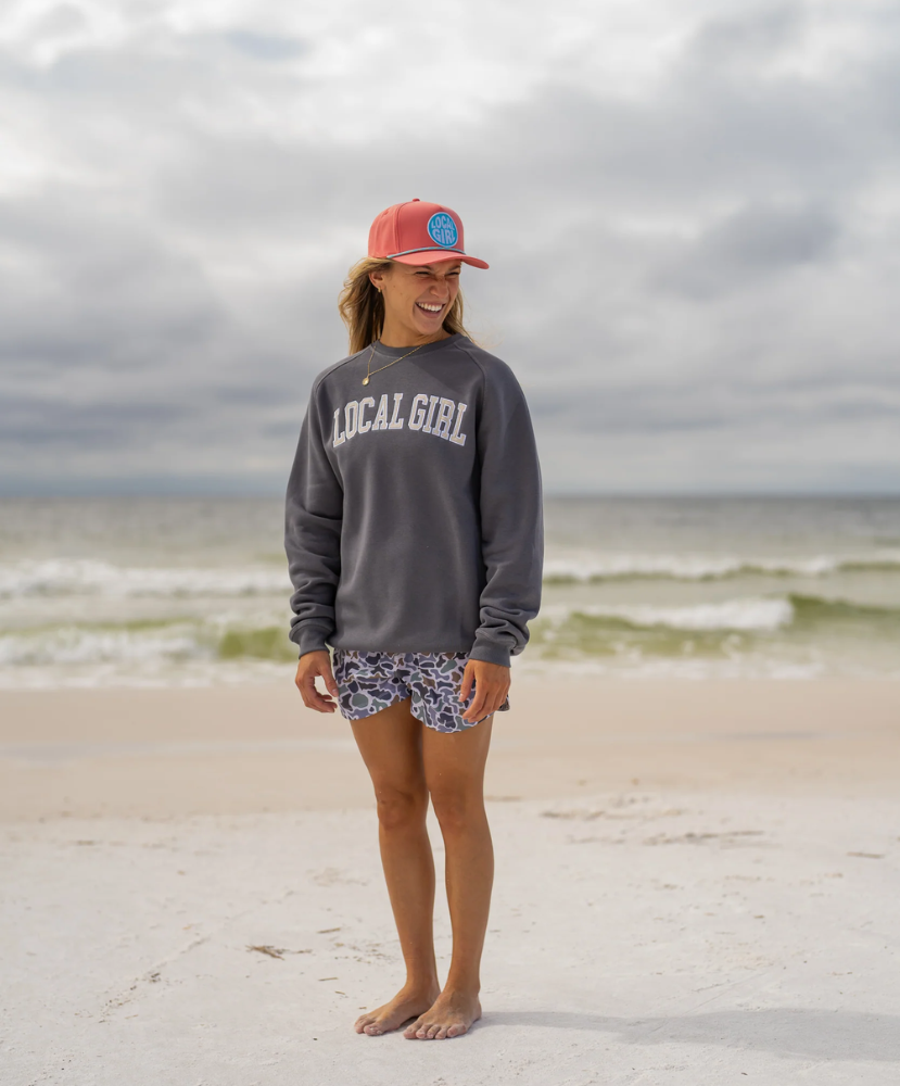Person wearing a 'Local Girl' sweatshirt and patterned shorts on a beach.