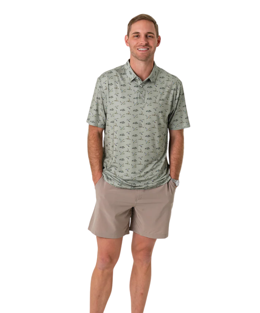 Man wearing a green flying duck patterned polo shirt and beige shorts on a white background