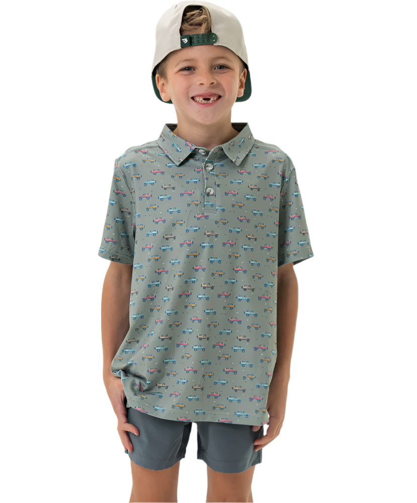 A young boy wearing a gray and blue PRINTED polo shirt with a collar, short sleeves, and light-colored shorts, smiling and posing for the camera.