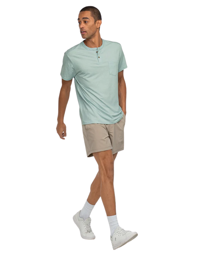 Man wearing a light green henley t-shirt and beige shorts on a white background