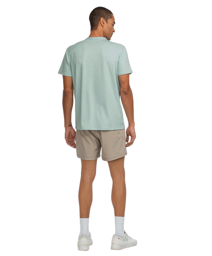 Man wearing a light green t-shirt and beige shorts on a white background