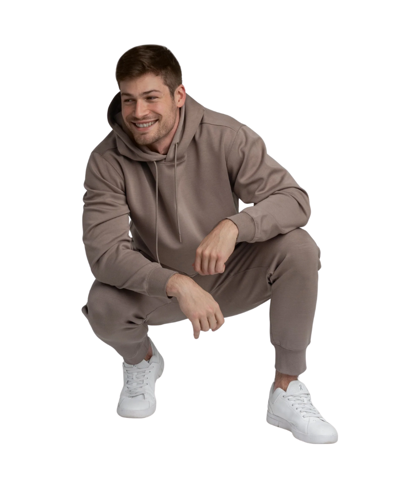 Man wearing a brown hoodie and jogger pants with white sneakers on a white background