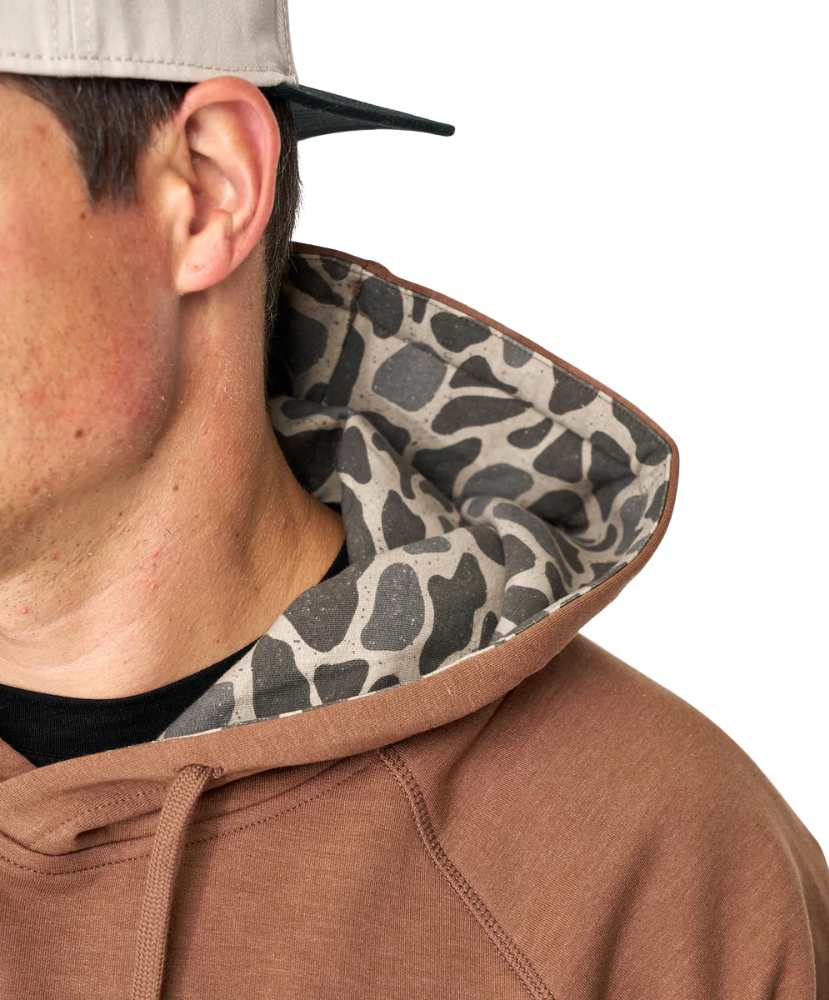 Close-up of a person wearing a brown hoodie with a camouflage hood lining on a white background