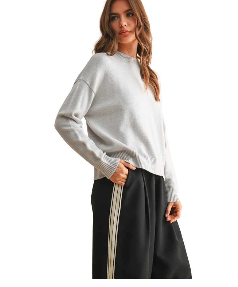 Woman wearing a light gray sweater and black pants with a white background