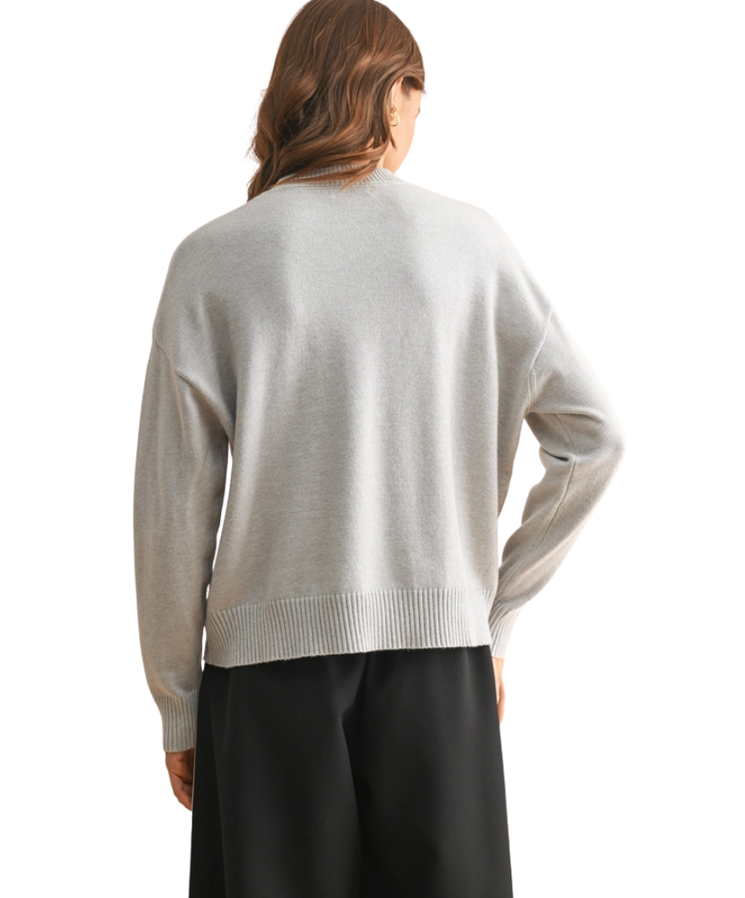 Person wearing a light gray sweater and black pants on a white background