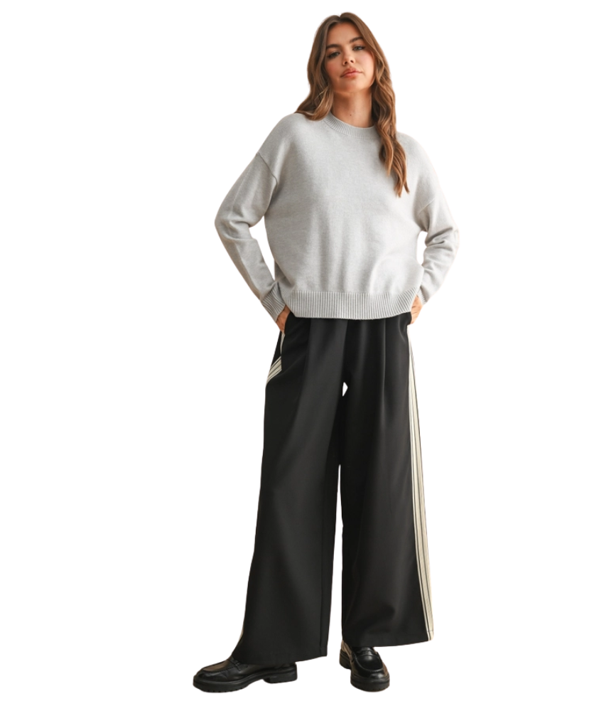 Woman wearing a white sweater and black pants with a stripe on a white background