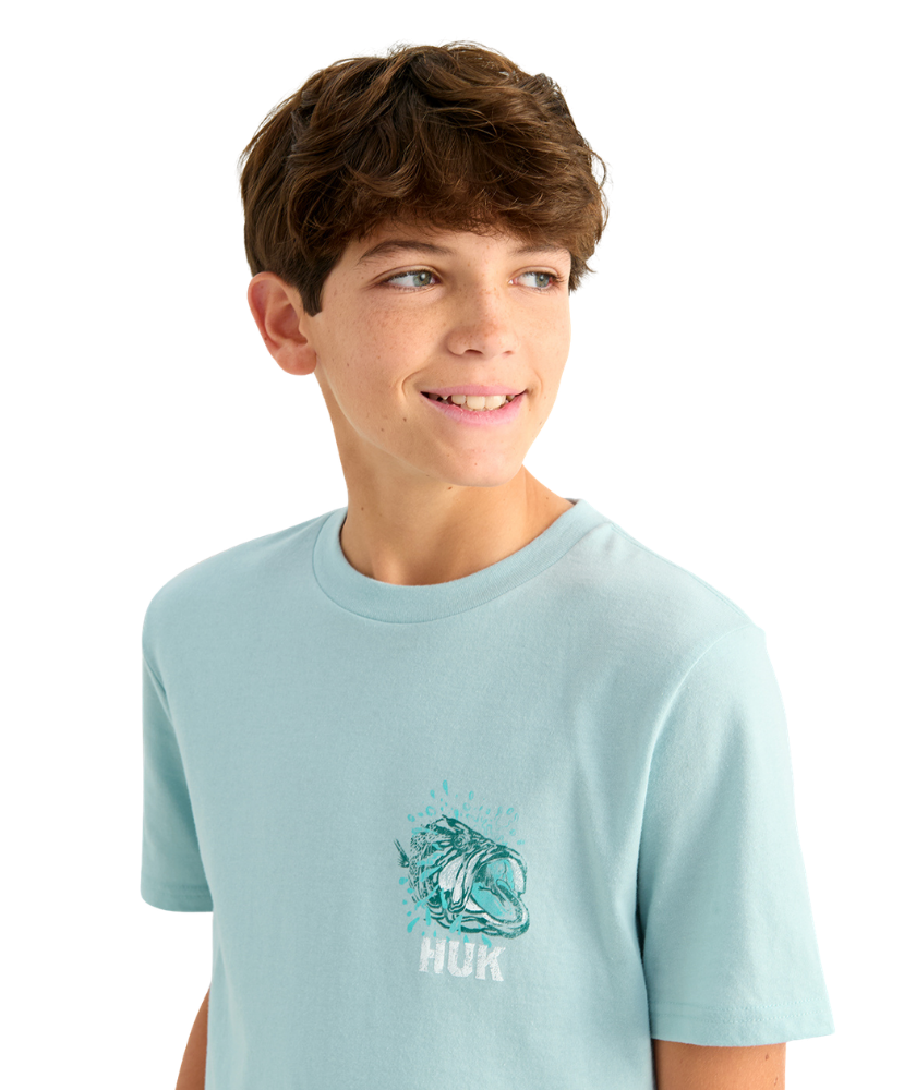 Young boy wearing a light blue HUK t-shirt with a graphic design of a bass on a white background