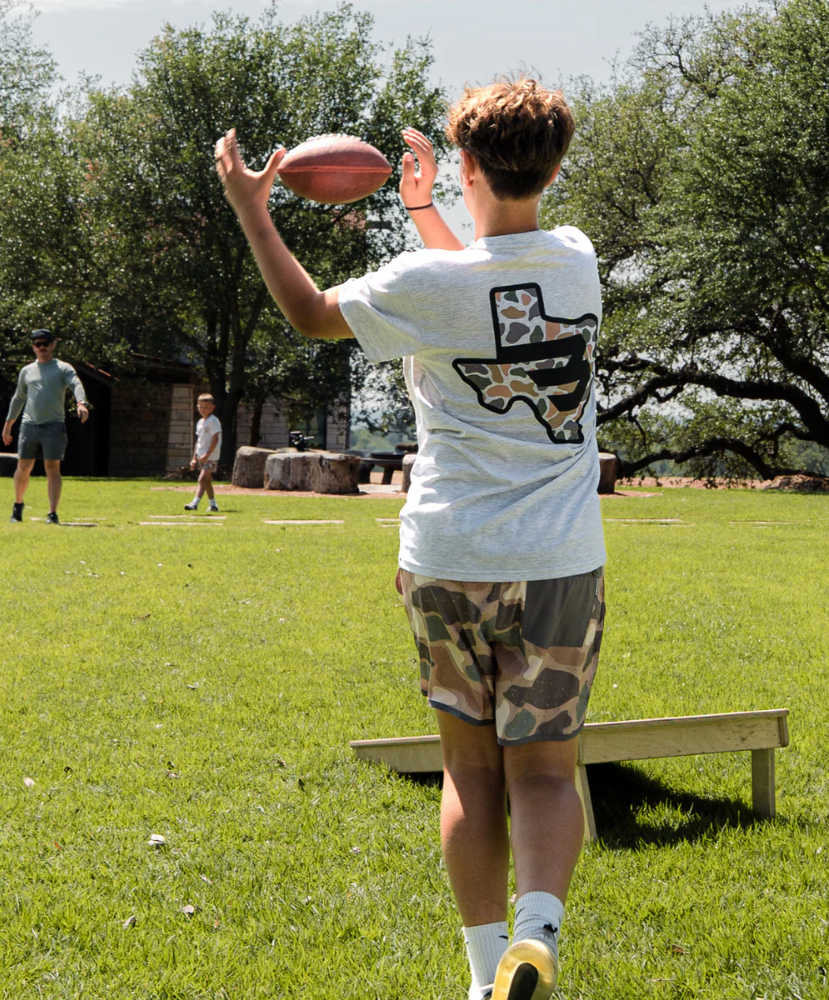 Person in a white t-shirt with a Texas design playing with a football on a grassy field.