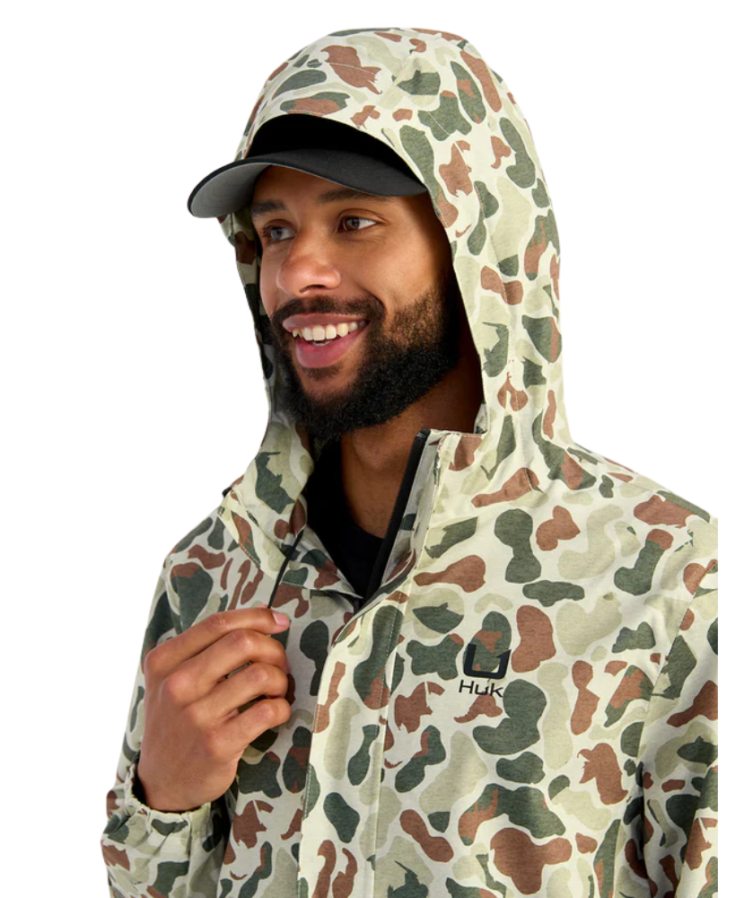 Man wearing a camouflage HUK jacket and hat on a white background
