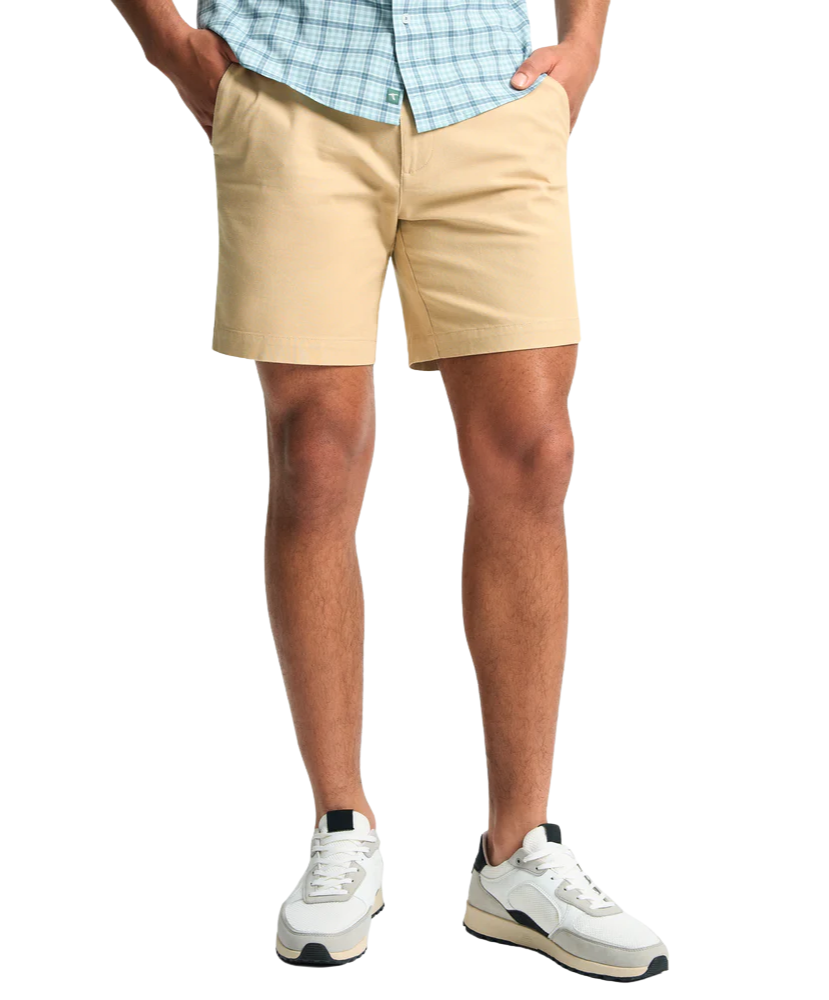 Person wearing beige shorts and white sneakers on a white background