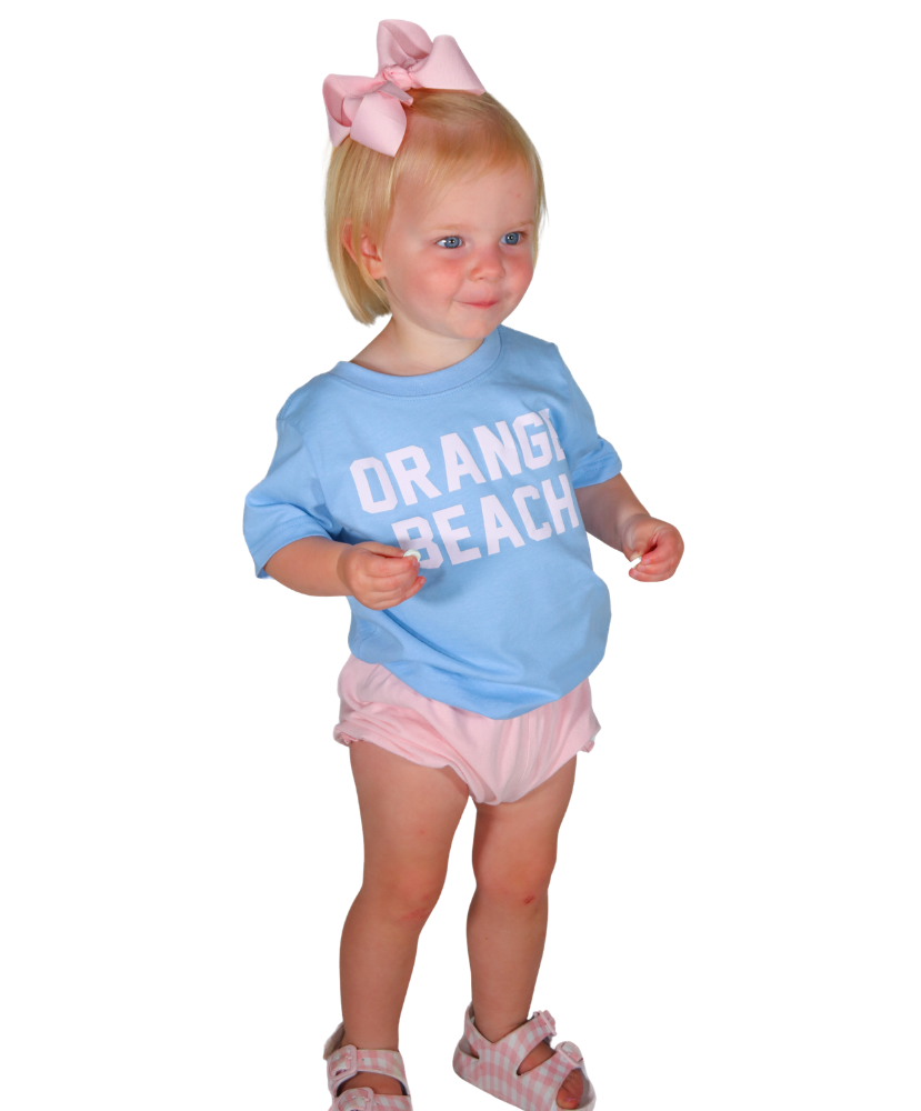Child wearing a blue shirt with 'Orange Beach' text and pink shorts on a white background