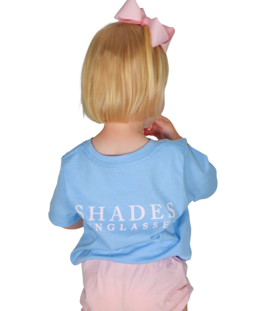 Child wearing a blue shirt with 'SHADES' text, standing against a white background