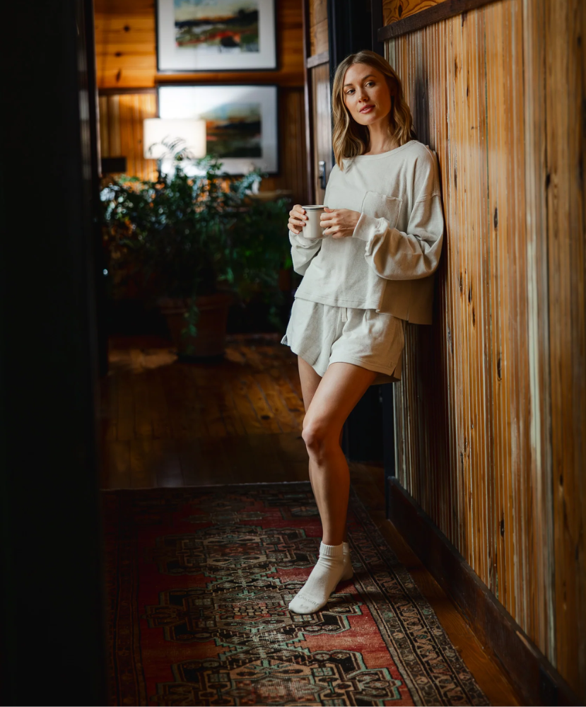 Woman in a cozy indoor setting holding a mug, wearing a light outfit.