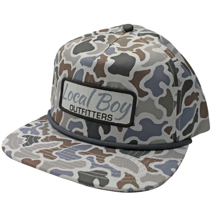 A flat-brim baseball cap with a gray, brown, and beige camouflage pattern, featuring a front patch that reads 'Local Boy OUTFITTERS'.