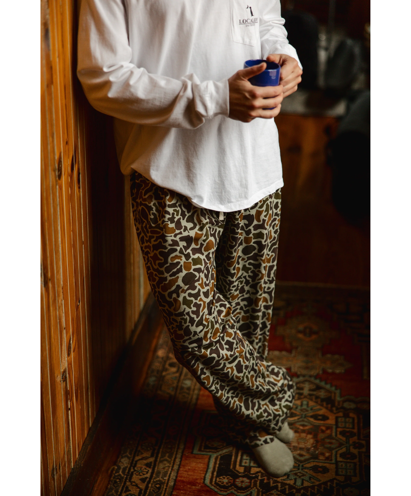 Person wearing a camo print pajama pants holding a blue coffee cup indoors.