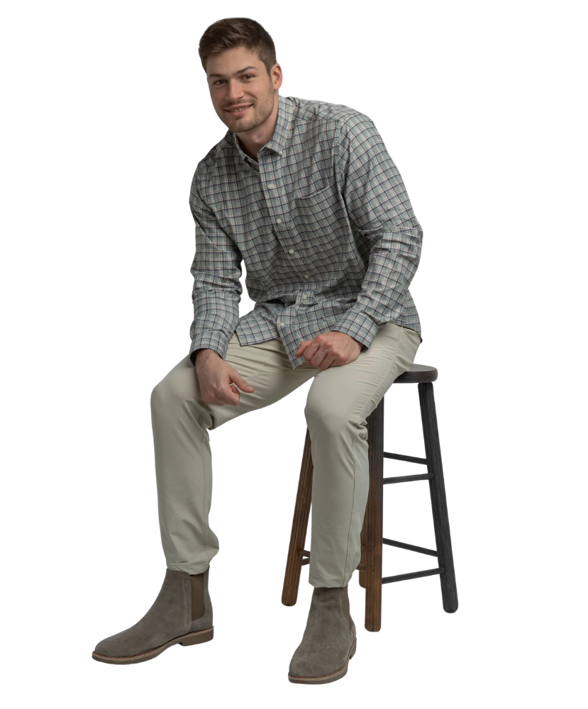 Man sitting on a stool wearing a plaid shirt, beige pants, and brown boots on a white background