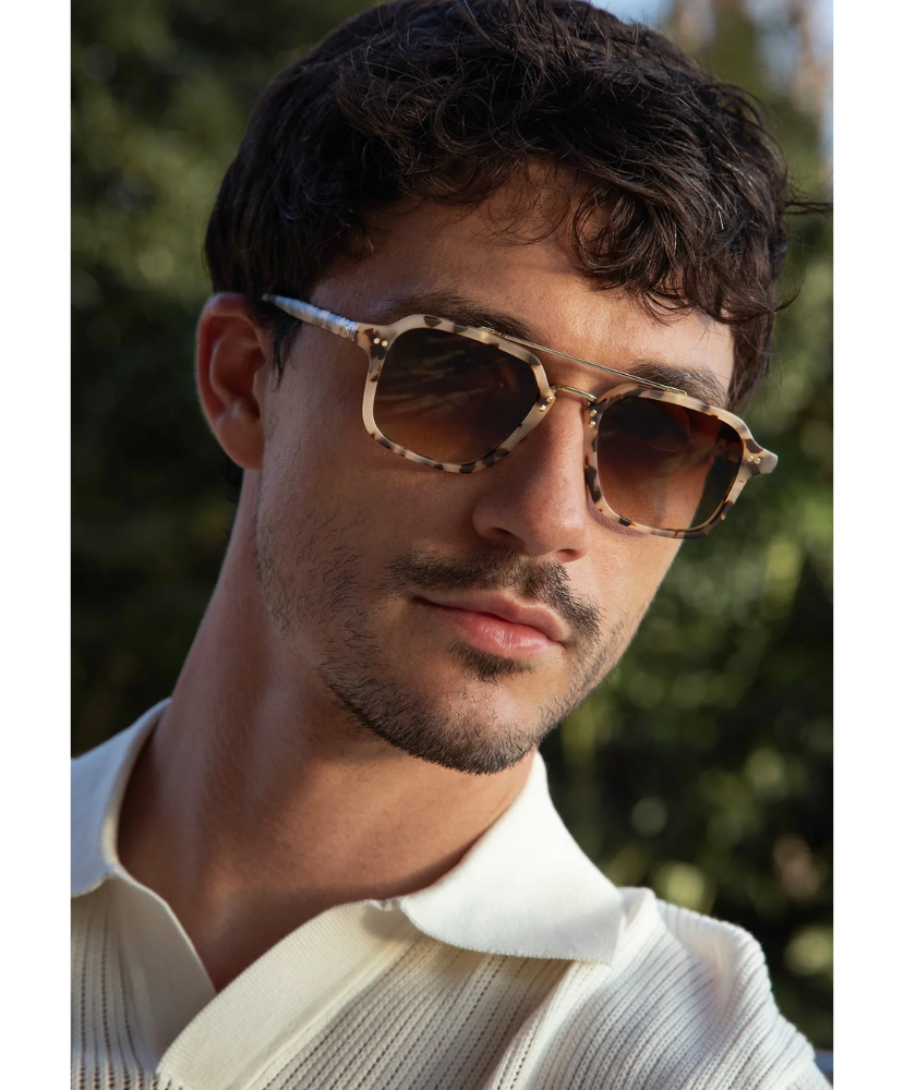 Man wearing tortoise Krewe print sunglasses with a blurred green background