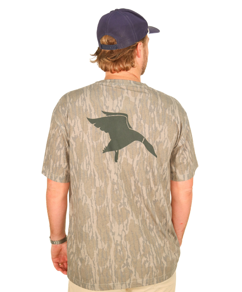 Man wearing a camouflage shirt with a duck design on the back, standing against a white background.