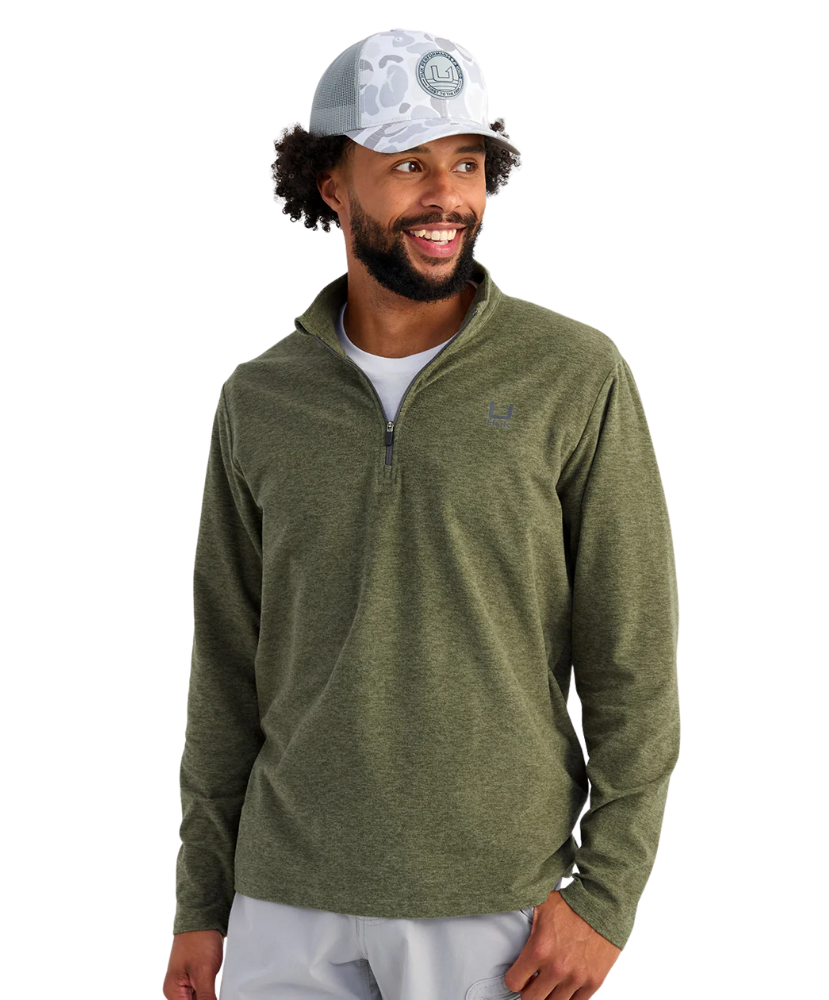 Man wearing a green HUK pullover and white cap on a white background