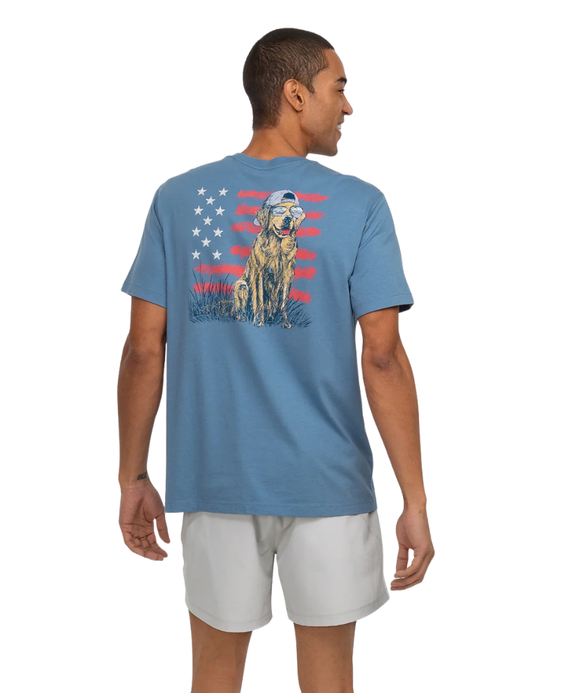 Man wearing a blue t-shirt with a graphic of a dog and American flag on the back, standing against a white background.