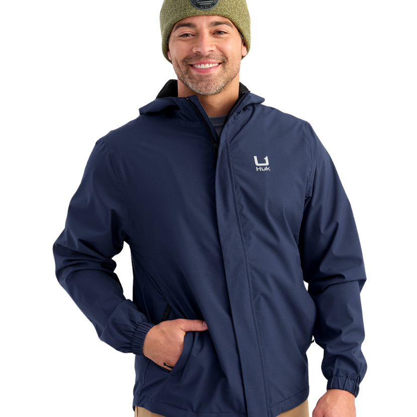 Man wearing a HUK navy jacket with a brand logo on a white background