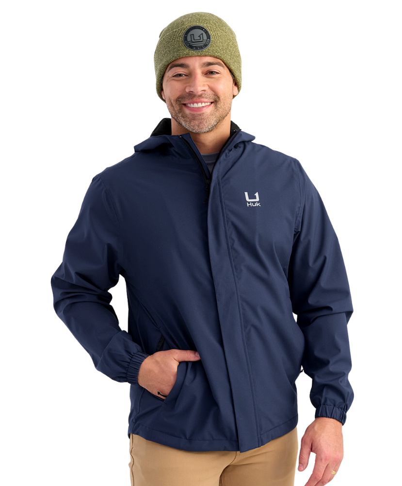 Man wearing a HUK navy jacket with a brand logo on a white background