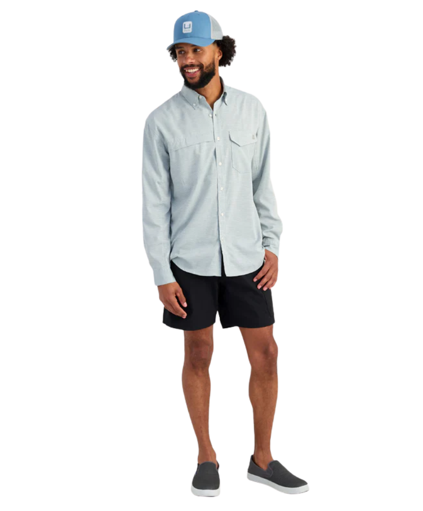 Man wearing a light blue HUK button-up shirt and blue cap on a white background