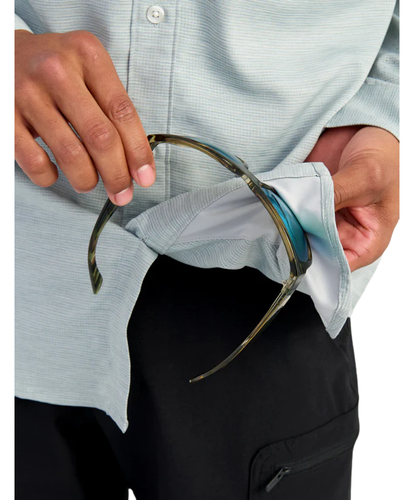Person cleaning a pair of glasses with a light blue button up Huk shirt and black pants.