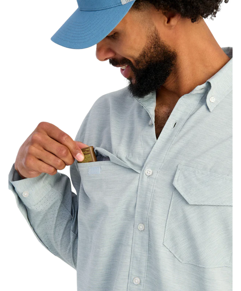 Man wearing a light blue shirt with a pocket, holding a small object.